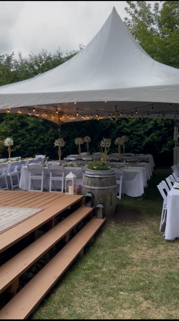 Decorated wedding reception under a Skytop tent with floral centerpieces and a wooden stage