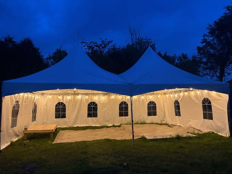 Skytop tent glowing with string lights at a backyard wedding reception at night