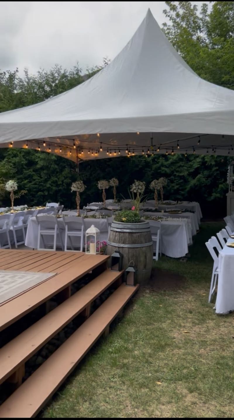 Decorated backyard wedding reception under a Skytop tent — white linens, floral centerpieces and string lights