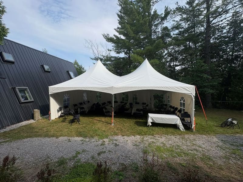 White peak tent set up on the lawn beside a house for a backyard party
